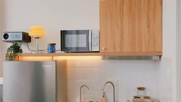 A compact kitchen with a built-in microwave, a stainless steel refrigerator, and a wooden cabinet above the sink.