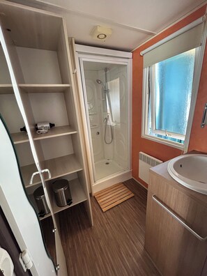 Een kleine badkamer met douche, wastafel en raam.