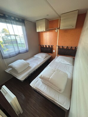 Een kamer met twee eenpersoonsbedden, een raam met gordijnen en een wandgemonteerde airconditioning.