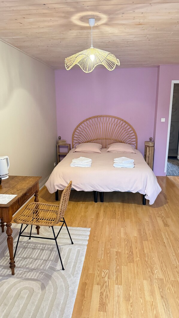 Un dormitorio con techo de madera, una cama con cabecero tejido, una mesita de noche, una silla y una lámpara colgante.