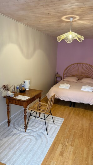 Un dormitorio con techo de madera, una cama con cabecera, una mesita de noche, una mesa con silla y una lámpara colgante.