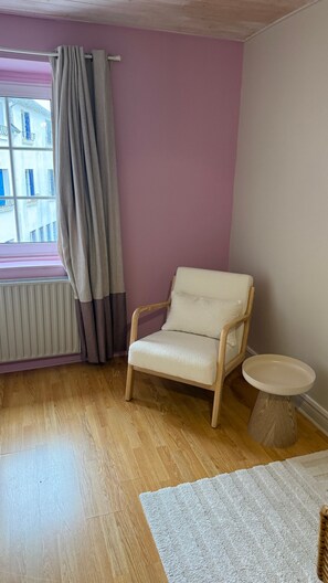 A room with a wooden floor, a beige armchair, a small round table, and a window with curtains. - Room Hortensi with Heated Pool May–September (Pont-Croix)