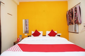 Une chambre d’hôtel comprenant un lit, une table de chevet, un miroir, une fenêtre avec des rideaux et un climatiseur fixé au mur.