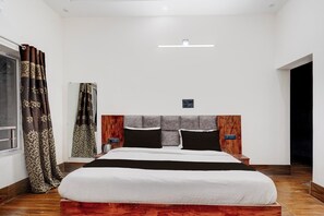 Une chambre à coucher avec un grand lit, une tête de lit en bois, une table de chevet et une commode, ainsi qu’une fenêtre avec des rideaux.