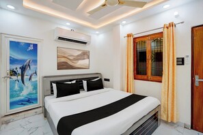 Une chambre d’hôtel avec un lit, un ventilateur de plafond, un appareil de climatisation, une fenêtre avec des rideaux et une porte.