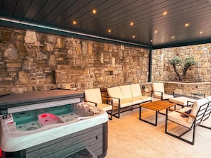 Un espacio al aire libre con paredes de piedra, jacuzzi, asientos y una mesa de madera.