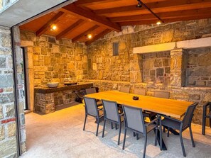 Una habitación de paredes de piedra con una mesa y sillas de madera, una chimenea de piedra y un ventanal pequeño.