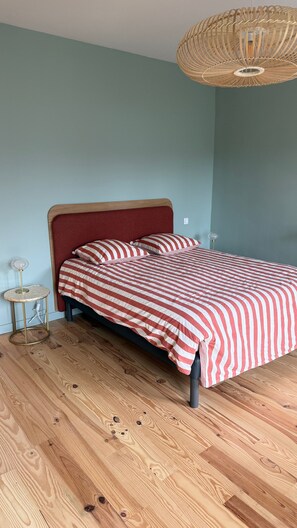 Un lit avec une couvre-lit à rayures, une lampe de chevet et un luminaire suspendu au plafond, fait de matériaux tressés.