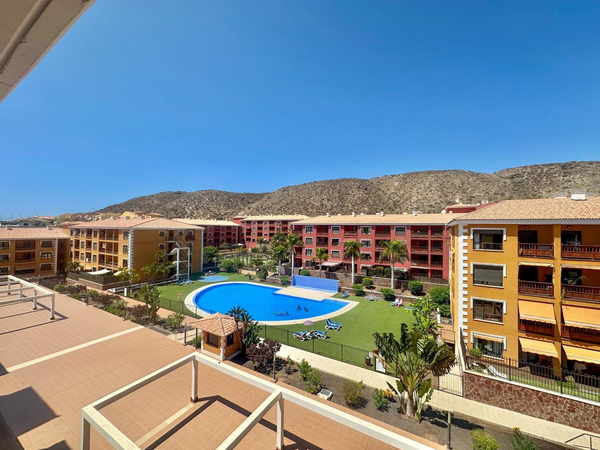 A hotel with a swimming pool, multiple balconies, and a view of the surrounding landscape.