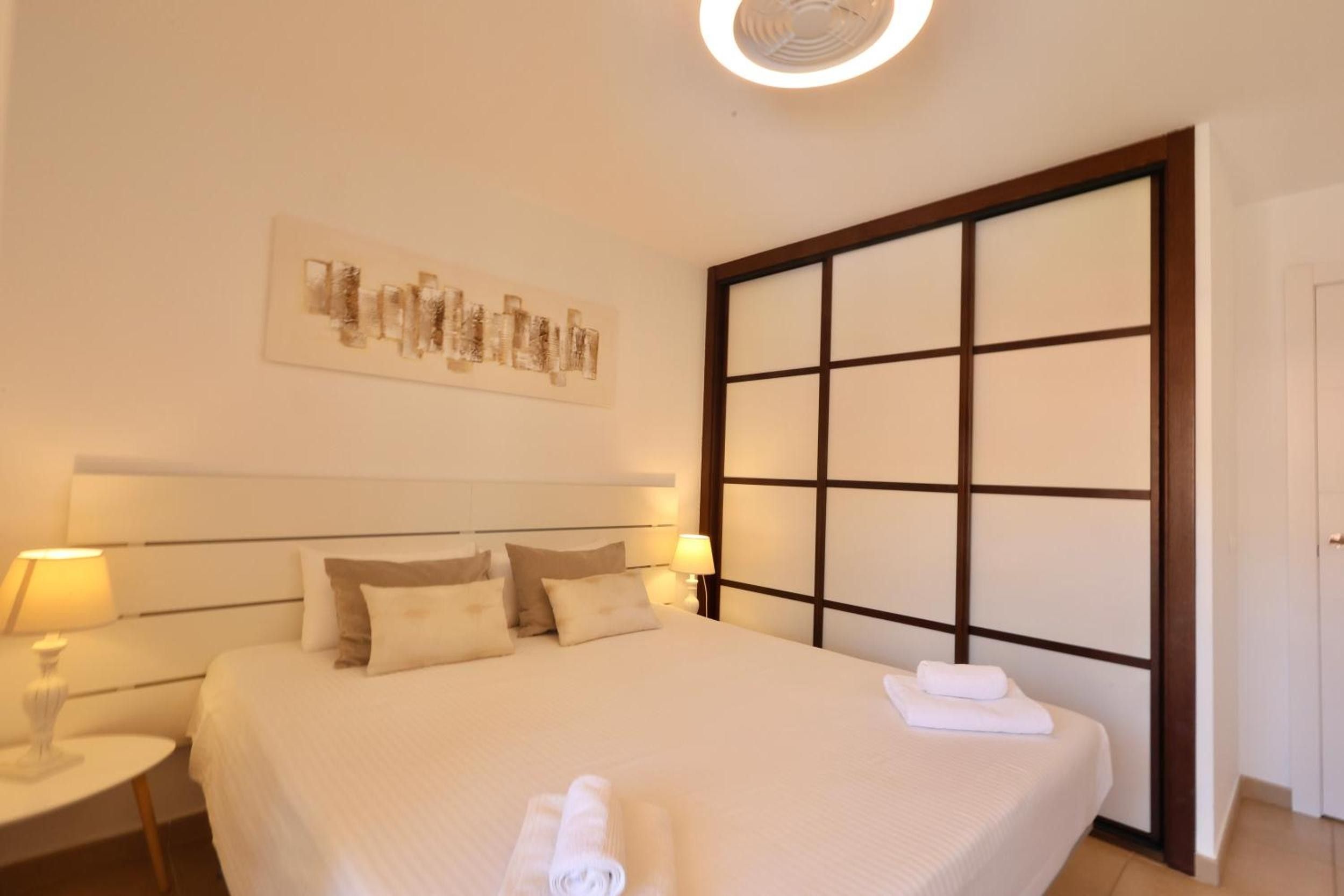 Una habitación de hotel con una cama grande, dos mesitas de noche con lámparas, una obra de arte en la pared y una puerta corredera.