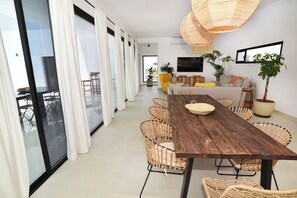 Un espace de vie moderne comprenant une table à manger en bois, des chaises en osier, un canapé et un téléviseur fixé au mur.