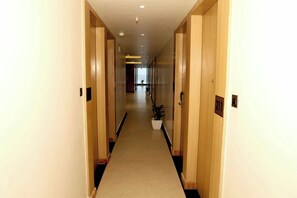 Un pasillo de hotel con puertas de madera, piso alfombrado y una planta en maceta.