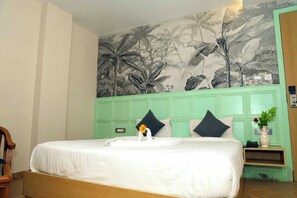 Une chambre d’hôtel avec un lit, une tête de lit verte, une fresque murale et une table de chevet sur laquelle se trouve un vase.