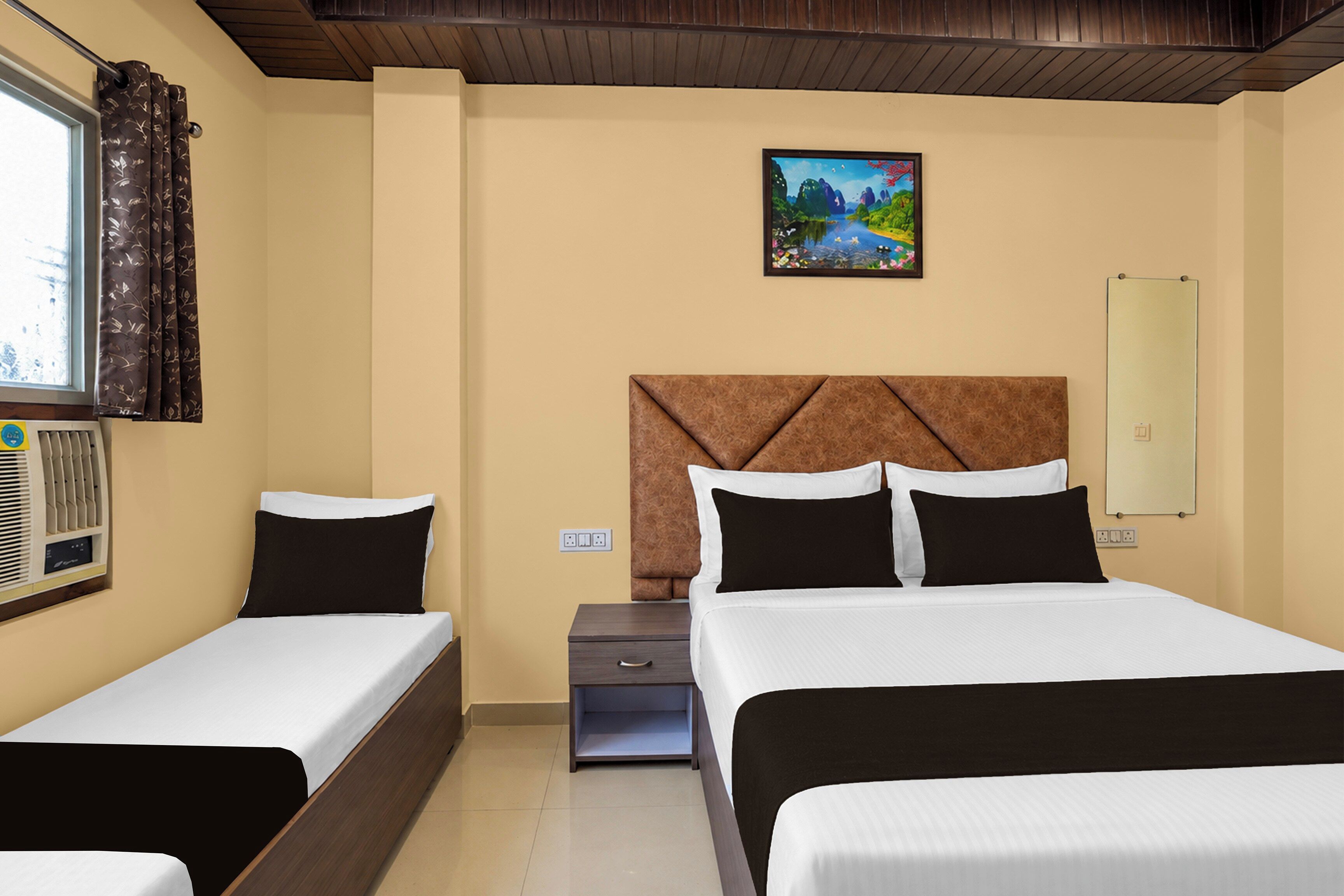 Habitación de hotel con dos camas, una mesita de noche, una pequeña mesa, un cuadro en la pared y una ventana con cortinas.
