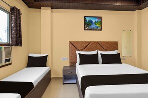 Une chambre d’hôtel avec deux lits, une table de chevet, une petite table, un tableau au mur et une fenêtre avec des rideaux.
