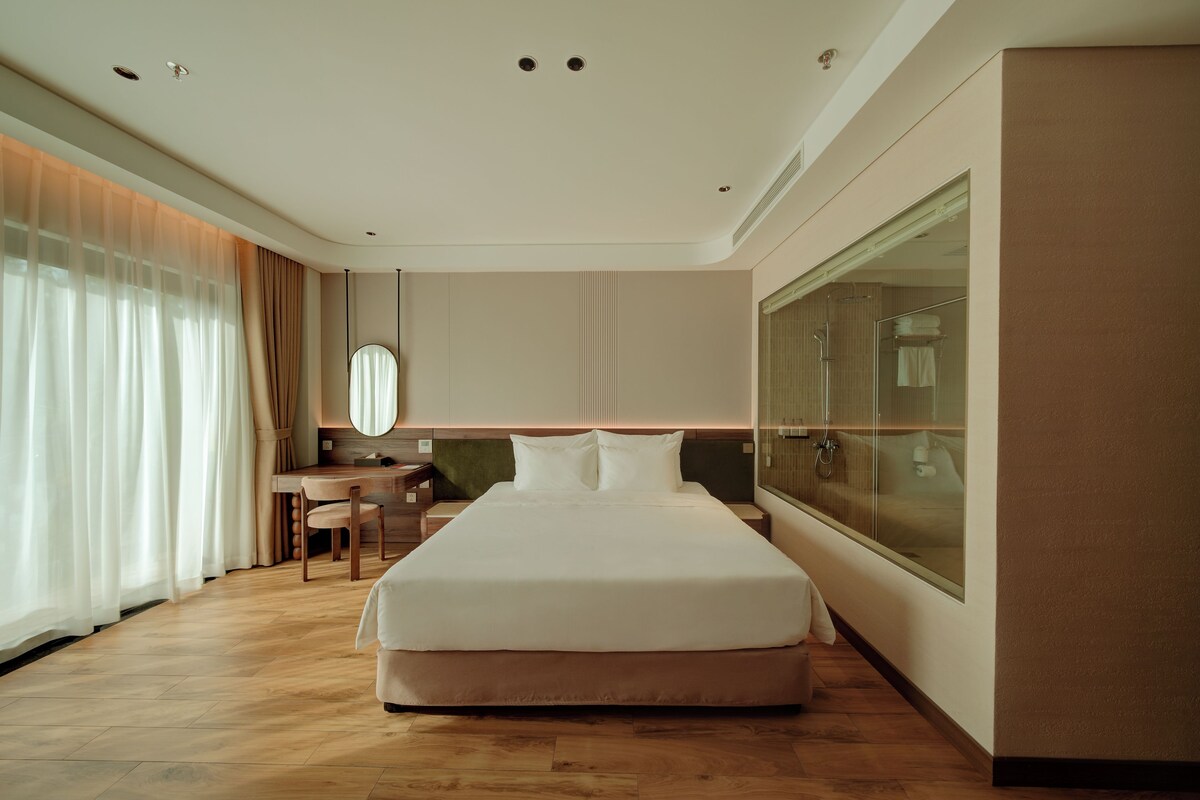 Een hotelkamer met een groot bed, een bureau, een stoel, een spiegel en een groot raam.