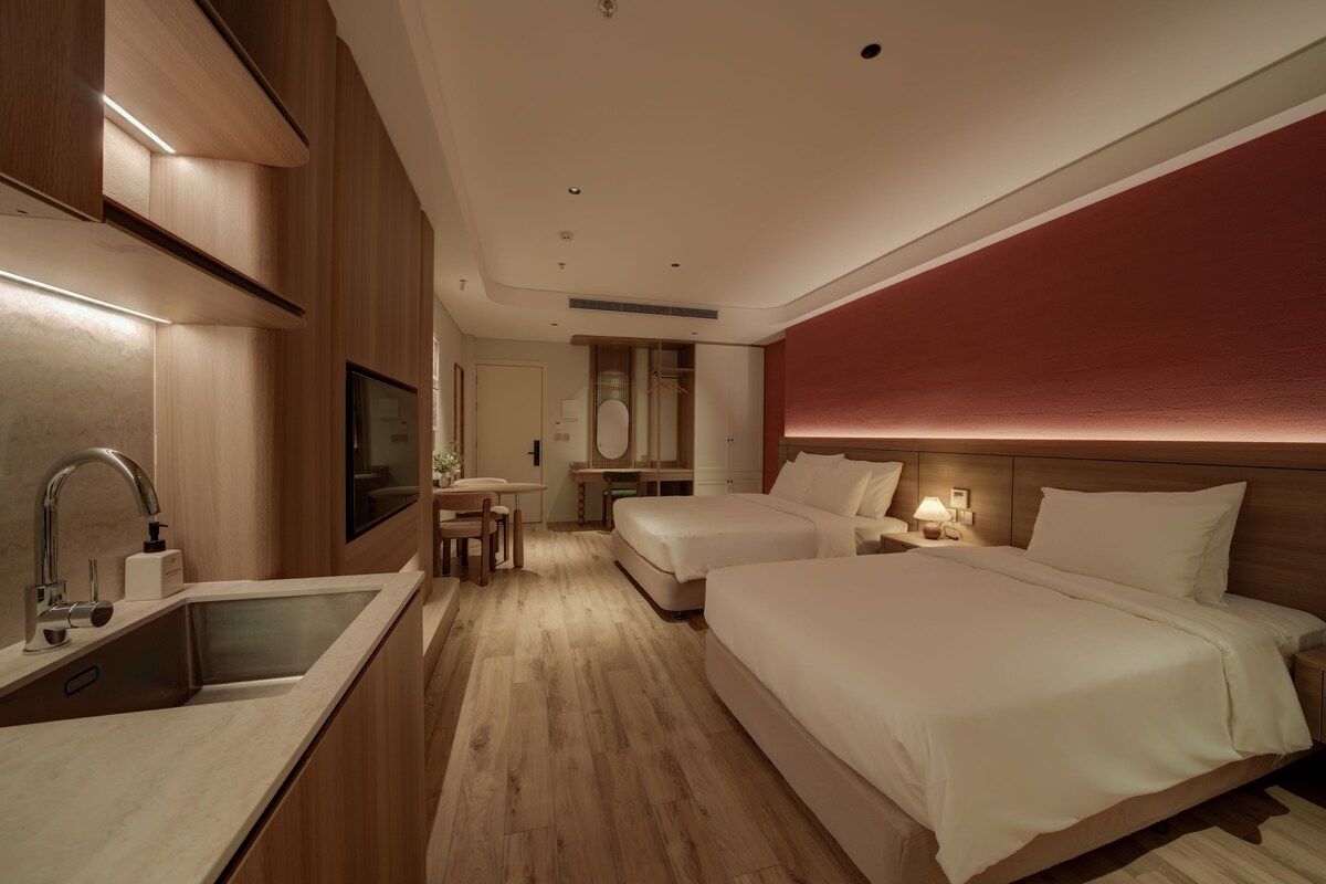 Een hotelkamer met houten vloer, een bed, een bureau, een stoel, een wastafel en een spiegel.