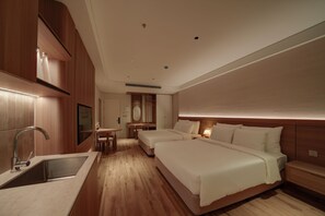 Een hotelkamer met een houten vloer, een bed, een bureau met stoel, een spiegel en een wastafel.