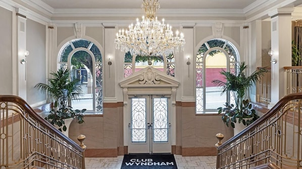 Uma entrada imponente com um candelabro, uma porta dupla e um tapete com a inscrição 'CLUB WYNDHAM'.