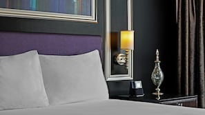 Quarto de hotel com cama, mesa de cabeceira, abajur e um vaso decorativo.