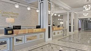 Uma área de recepção de hotel com design moderno, com balcão de atendimento, sinalização na parede e luminárias elegantes.