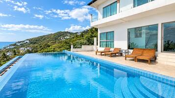 Un área de piscina moderna con vista despejada al océano y una ladera.