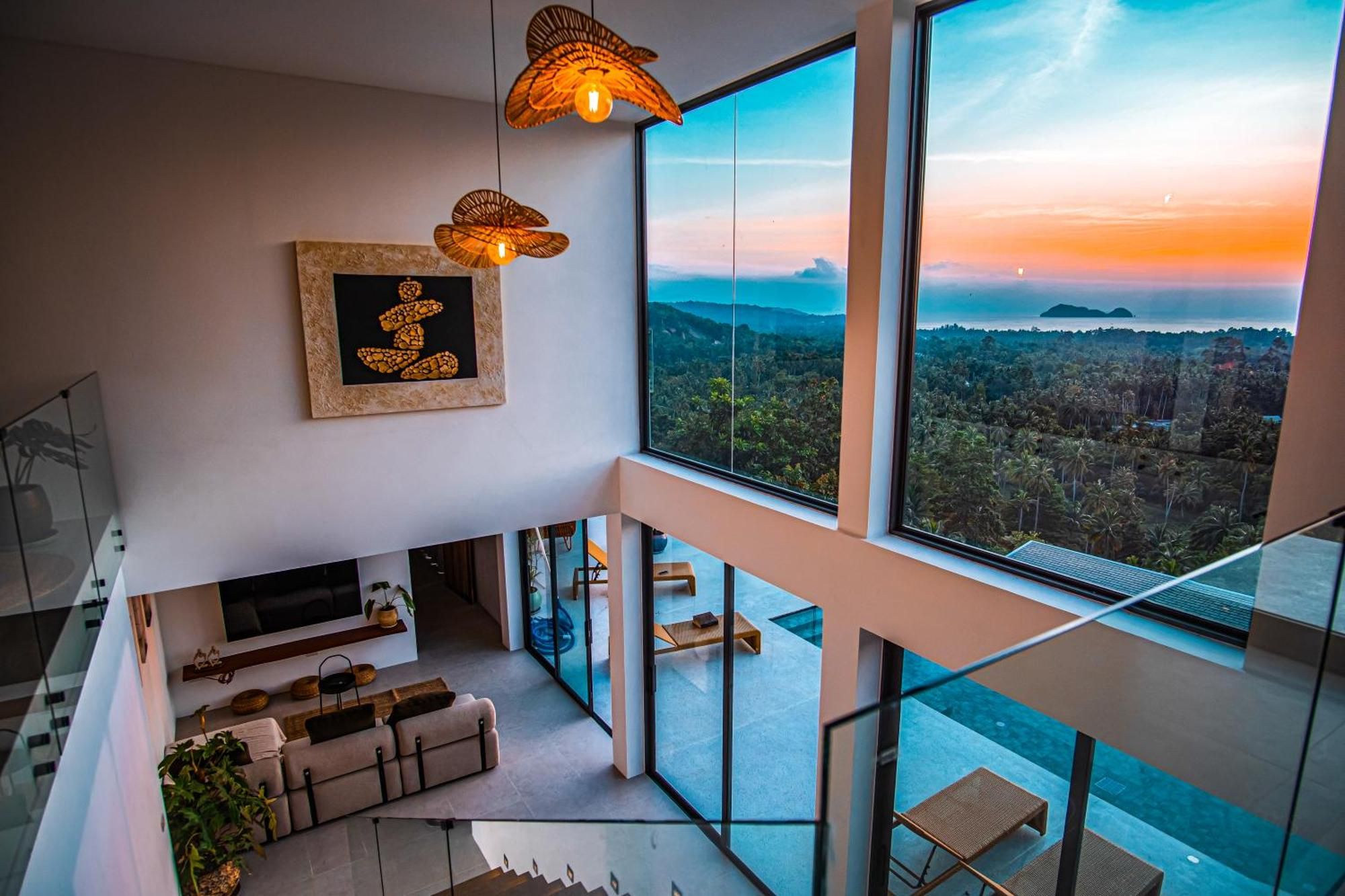 Un interior moderno con un gran ventanal que da a un paisaje, un sofá y una obra de arte enmarcada.