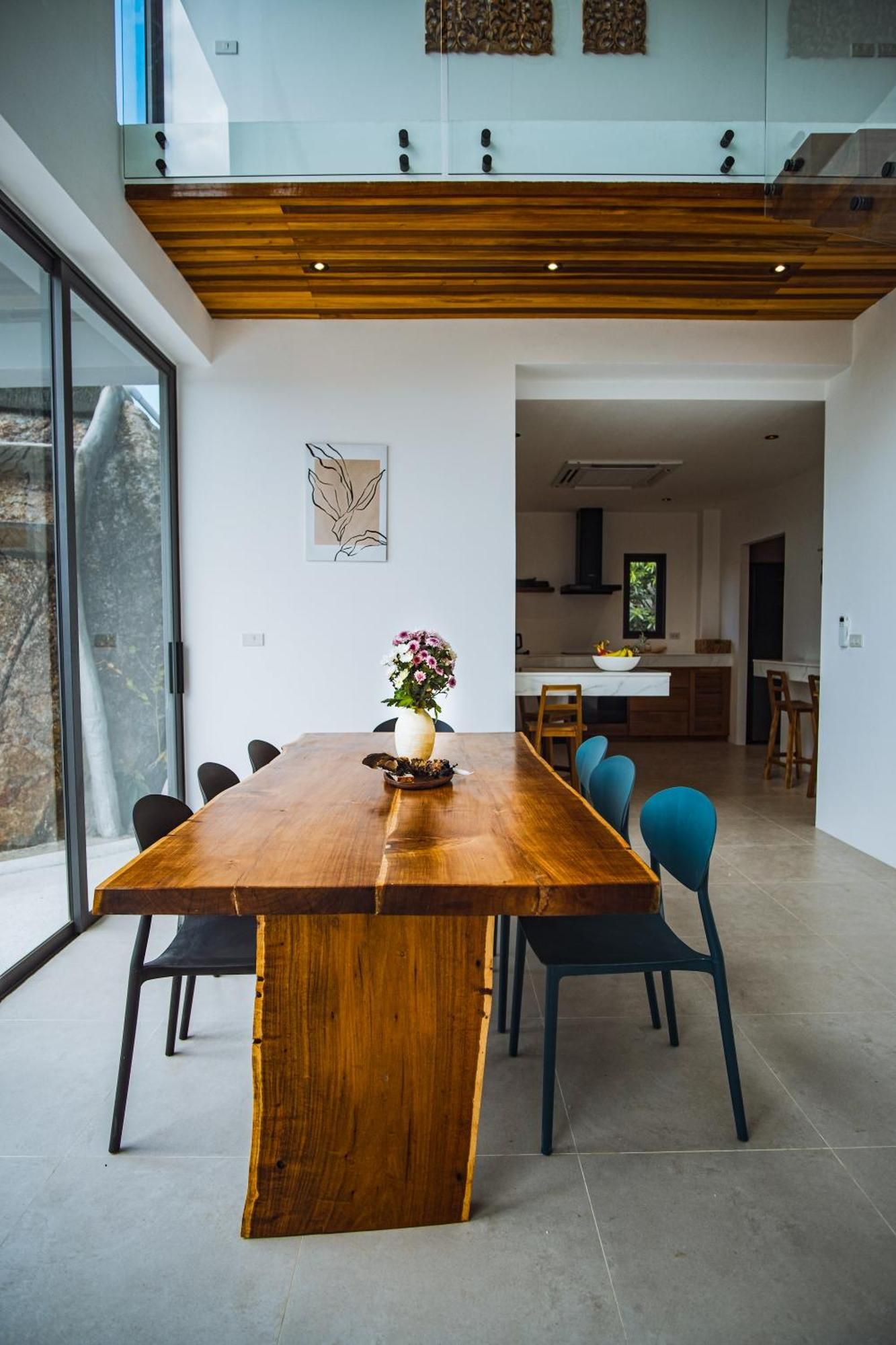 Un espace repas moderne avec une grande table en bois, des chaises bleues et un vase rempli de fleurs.