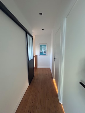 Un pasillo con suelo de madera, paredes blancas y un cuadro en la pared.