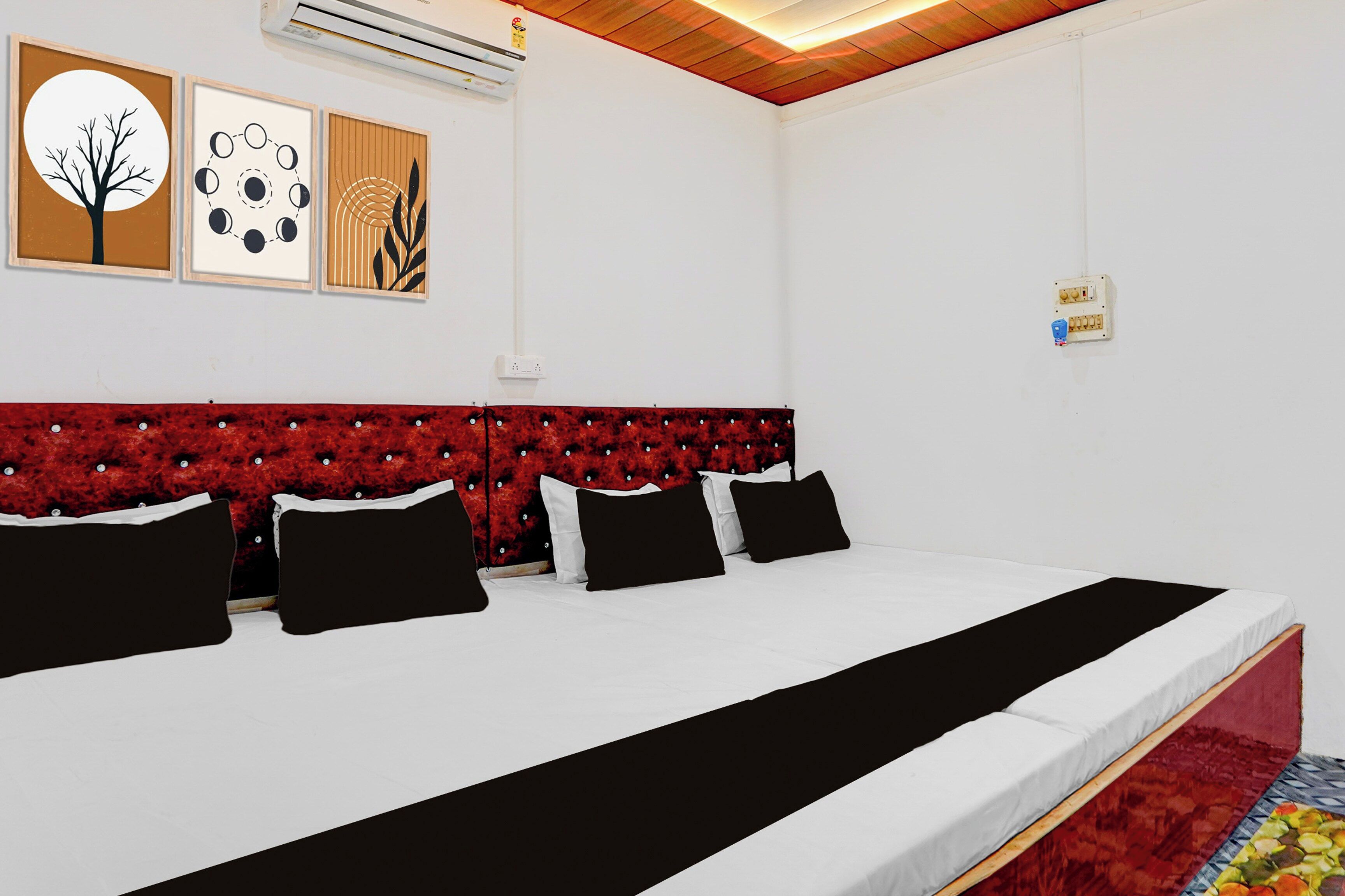 Une chambre d’hôtel avec un grand lit, une tête de lit rouge en tissu et des climatiseurs fixés au mur.