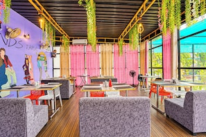 L’intérieur d’un restaurant, avec des tables, des chaises, des plantes suspendues et une fresque murale.