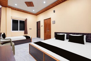 Ein Hotelzimmer mit einem großen Bett, einem kleineren Bett, einem Schreibtisch und einem Fenster mit Vorhängen.