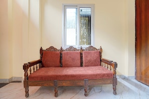 A wooden sofa with a cushioned seat and backrest, positioned in front of a window with decorative glass panes. - Hotel O Kashi Dham River View (Varanasi)