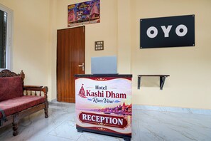 Ein Empfangsbereich mit einem Schild für das Hotel Kashi Dham River View, einer hölzernen Bank und einer Tür.