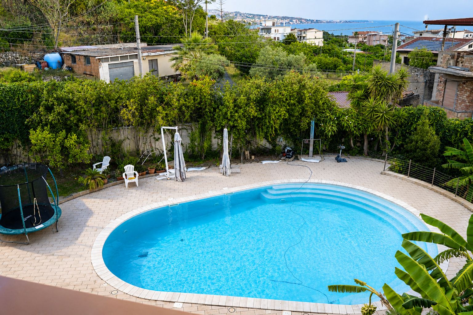 Una piscina con bordo in mattoni, immersa nel verde e con vista sul mare.