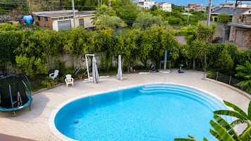 Una piscina con bordo in mattoni, immersa nel verde e con vista sul mare.
