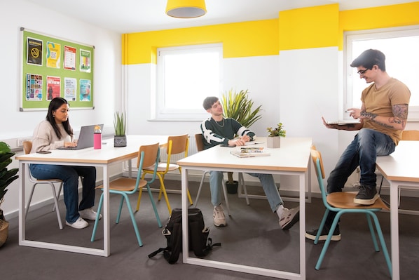 A modern meeting room with white tables, colorful chairs, and a bulletin board with safety and fire prevention notices. - Student Only William Murdoch (Birmingham)