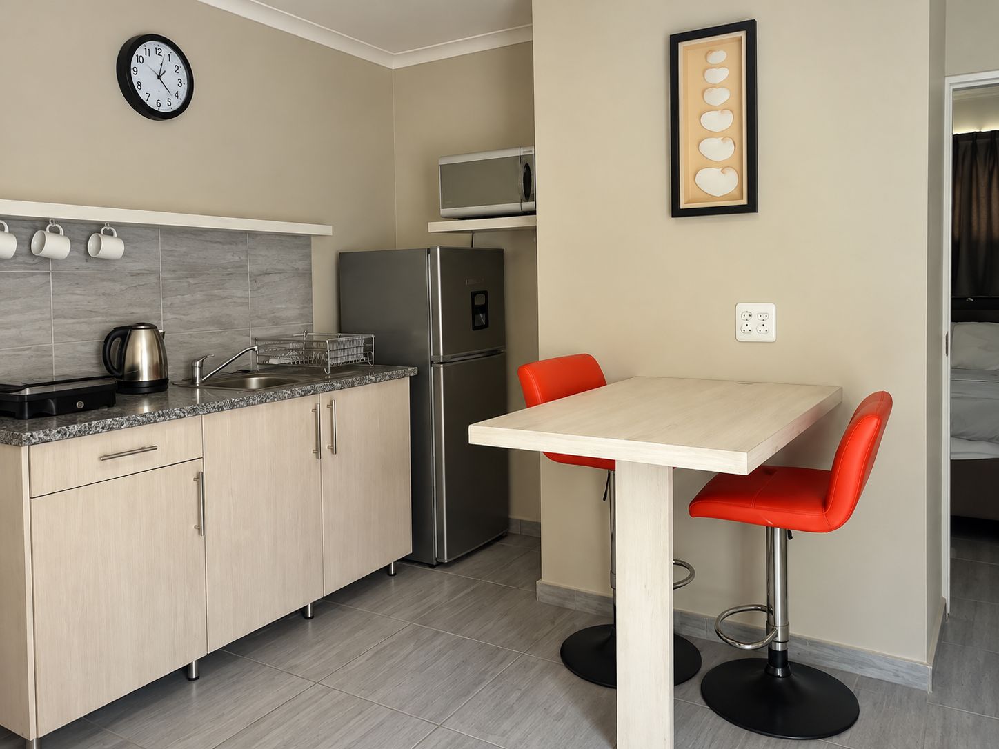 A compact kitchen with a refrigerator, microwave, and a clock on the wall.