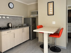 A compact kitchen with a refrigerator, microwave, and a clock on the wall. - Omaruru Street (Henties Bay)