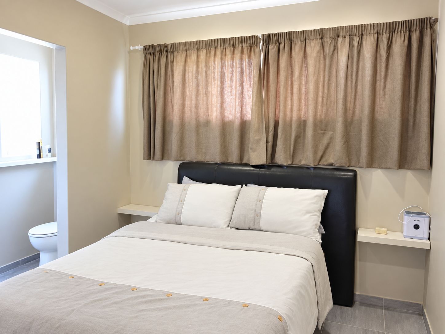 A bedroom with a bed, a headboard, a window with curtains, a bedside table, and a nightstand.
