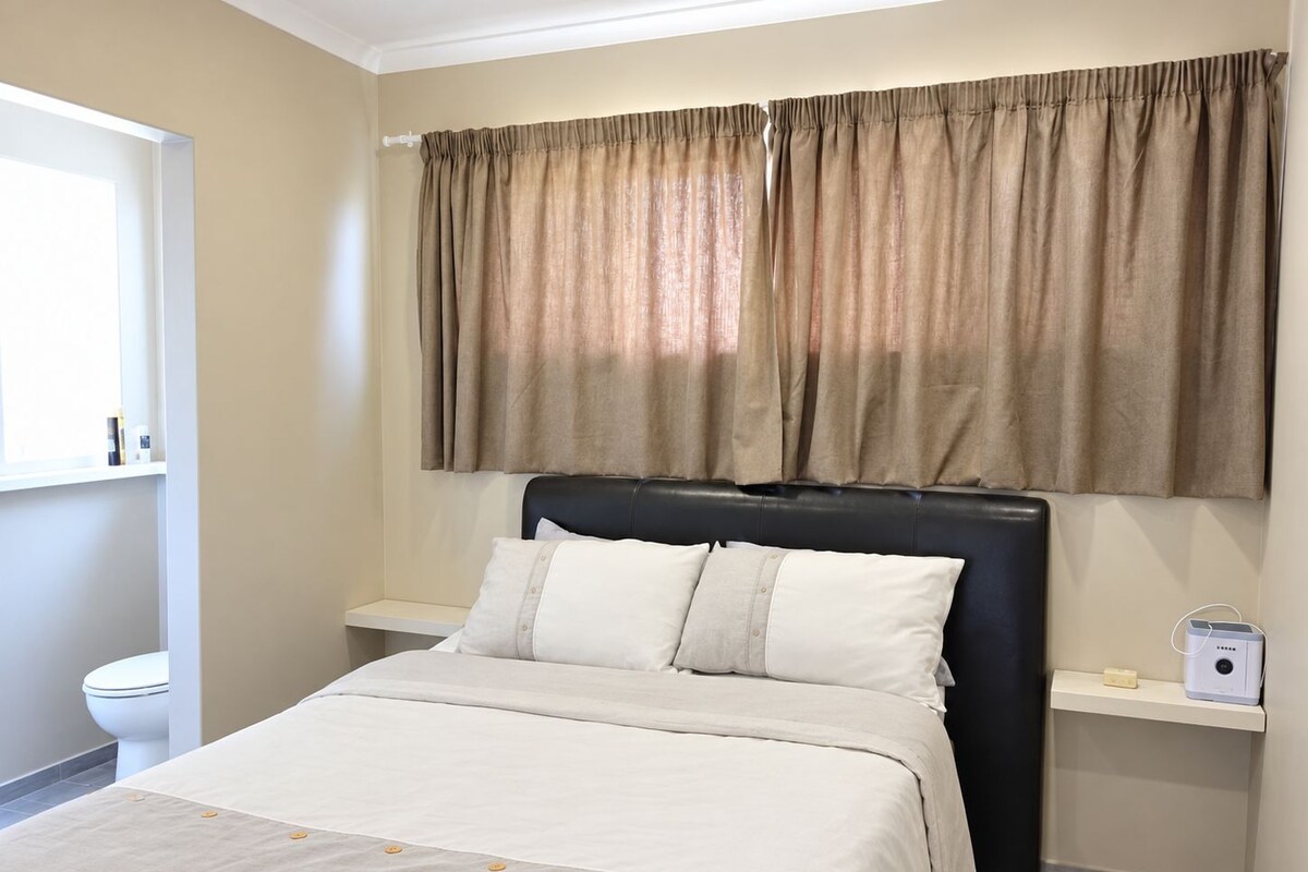 A bedroom with a bed, a headboard, a window with curtains, a bedside table, and a nightstand.