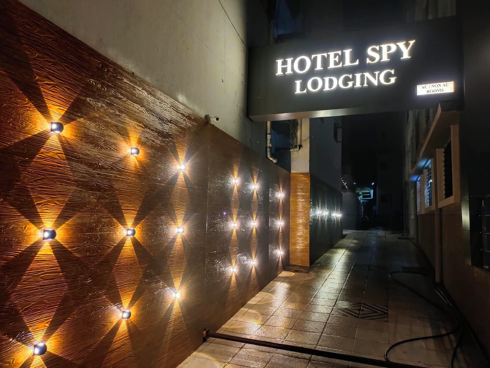 Un couloir avec une enseigne indiquant « Hotel Spy Lodging », agrémenté d’un motif géométrique sur le mur et d’un éclairage décoratif.