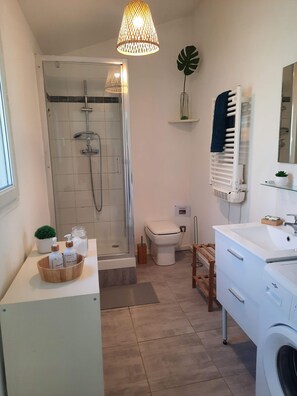 Une salle de bain moderne avec une douche à parois de verre, un lavabo blanc, des toilettes et un lave-linge.