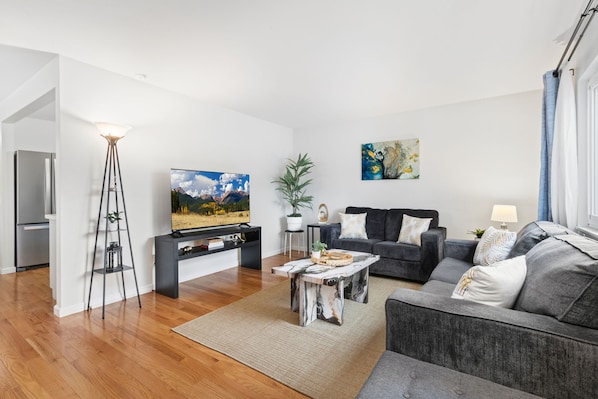 Uma sala de estar moderna com televisão de tela plana, sofá, mesa de centro e luminária de chão.