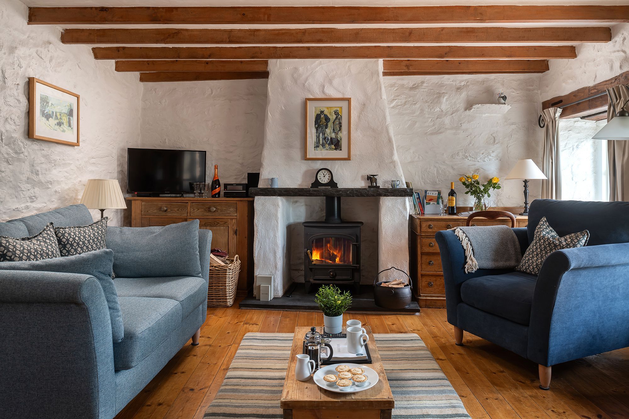 Una sala de estar acogedora con chimenea, sofás, una mesita de centro con pasteles y un televisor.
