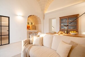 A modern living room with a sofa, a wooden cabinet, and a kitchen area in the background. - Casa Cactus | Stylish Home with Private Rooftop Terrace (Carovigno)