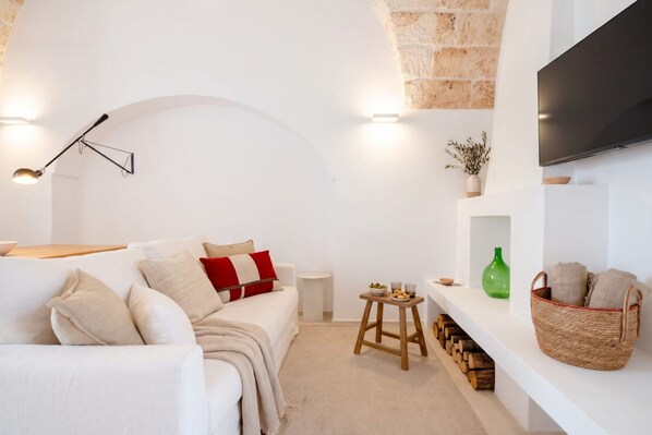 A modern living room with a white sofa, a small wooden stool, and a television mounted on the wall. - Casa Cactus | Stylish Home with Private Rooftop Terrace (Carovigno)