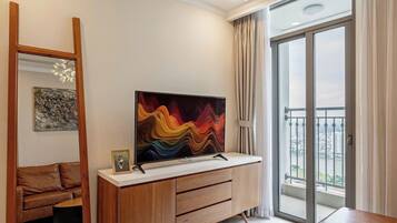 A modern living room with a large flat-screen TV, a wooden coffee table, and a balcony with a view.