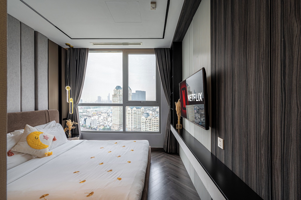 A hotel room with a large bed, a city view, a TV on the wall, and a modern design.