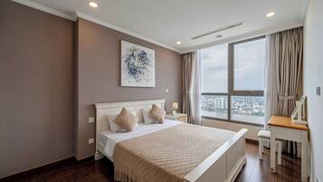 A hotel room with a large bed, a desk, a chair, a window with a city view, and a ceiling light.